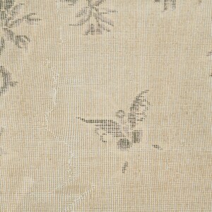 May include: Close-up of a beige rug with a floral pattern and a butterfly design. The rug has a distressed look with faded colors and a textured surface. The floral and butterfly motifs are in shades of gray.