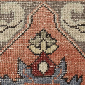 May include: Close-up of a red, gray, and beige patterned rug with a central design of a stylized plant with a red base. The rug has a woven texture.