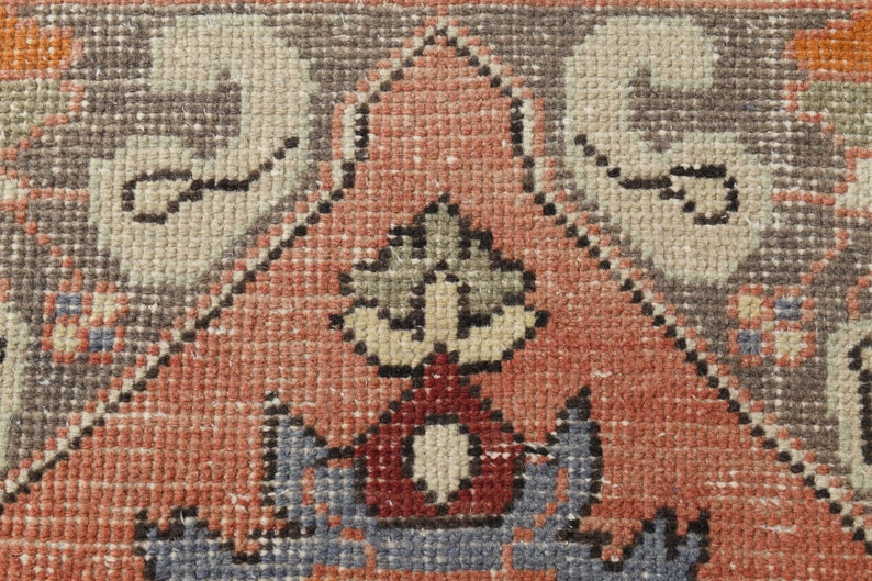 May include: Close-up of a red, gray, and beige patterned rug with a central design of a stylized plant with a red base. The rug has a woven texture.
