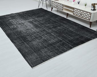 May include: A large, rectangular black rug with a distressed, faded appearance. The rug has a textured surface with lighter gray areas, creating a vintage or antique look. The rug is placed on a white floor.