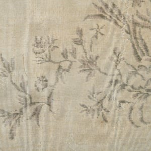 May include: Close-up of a beige rug with a floral pattern in shades of brown. The design features stylized flowers and foliage, creating a vintage or antique aesthetic. The rug's texture is visible, suggesting a woven construction.