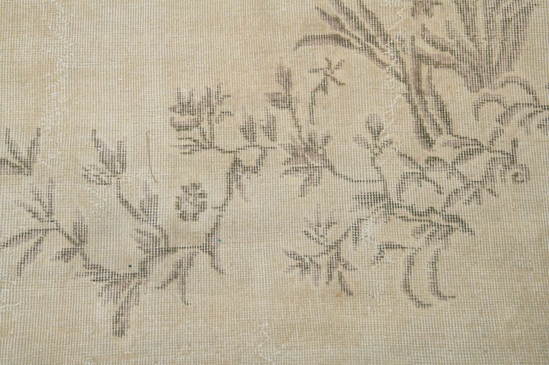 May include: Close-up of a beige rug with a floral pattern in shades of brown. The design features stylized flowers and foliage, creating a vintage or antique aesthetic. The rug's texture is visible, suggesting a woven construction.