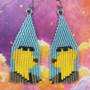 May include: A pair of dangle earrings featuring a triangular beaded design. The beads are light blue, yellow, black, and gray, arranged to form a stylized bird figure. Each earring hangs from a silver-toned metal hook and includes a fringe of beads.