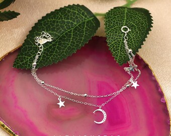 May include: A silver double-layered anklet with star and crescent moon charms. The anklet features small beads and dangling stars. The image is set against a pink and green background, with the text "ALTAIRXSTAR Handcrafted Jeweller".