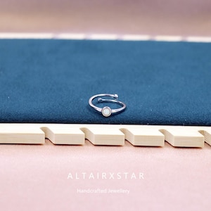 May include: A silver-toned adjustable ring with a small, round, white opal stone. The ring is set against a dark teal background, with the brand name "ALTAIRXSTAR" and the text "Handcrafted Jewellery" visible below.