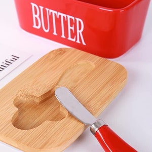 May include: Red ceramic butter dish with the word "BUTTER" in white lettering. The dish has a wooden lid with a cutout for a butter knife. A red-handled butter knife is included.