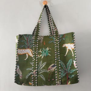 Könnte beinhalten: Grüne Tragetasche mit Dschungel-Print mit Leoparden, Zebras und tropischen Pflanzen. Die Tasche hat eine gesteppte Textur und gestreifte Akzente in Rosa und Weiß. Die Griffe sind grün mit gestreiften Details.