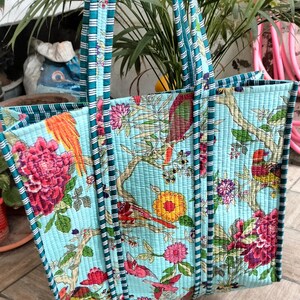 May include: A light blue tote bag with a floral print featuring birds and flowers. The bag has teal and white striped handles.
