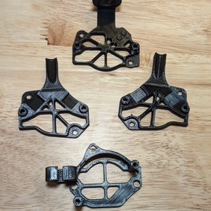 May include: Four black 3D printed parts for a drone or other device. The parts are made of a strong, durable plastic and have a variety of intricate details.