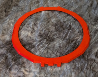 Puede incluir: Un anillo circular de plástico rojo brillante con un diseño geométrico. El anillo tiene una superficie ligeramente texturizada y parece estar hecho de un material duradero.