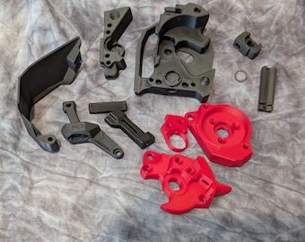 Puede incluir: Surtido de piezas impresas en 3D de color negro y rojo para una pistola de modelo. Las piezas incluyen un marco, un cañón, una empuñadura y un cargador. Las piezas están hechas de plástico y tienen un acabado liso.