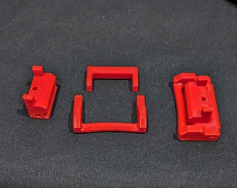 Op de afbeelding: Drie rode plastic onderdelen voor een 3D-geprint modelpakket. De onderdelen zijn in de vorm van een rechthoek, een vierkant en een klein doosje.