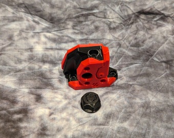May include: A red and black plastic 3D printed part with a hexagonal nut. The part has several holes and a textured surface.