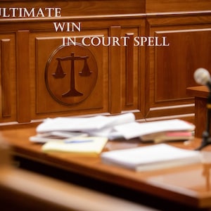 May include: A wooden courtroom bench with a scale of justice carved into the front. The bench is in a courtroom with a microphone on a stand and papers on a table in the foreground.