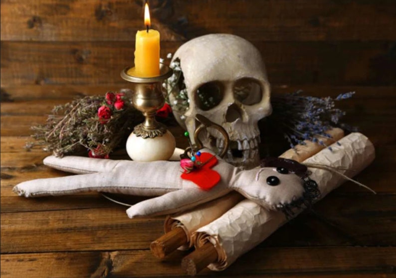 May include: A white human skull with a lit candle in a brass candlestick, a red heart with pins, and two rolled up scrolls on a wooden surface.