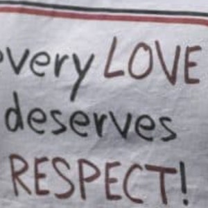May include: A white sign with a red border and black text that reads "every LOVE deserves RESPECT!"
