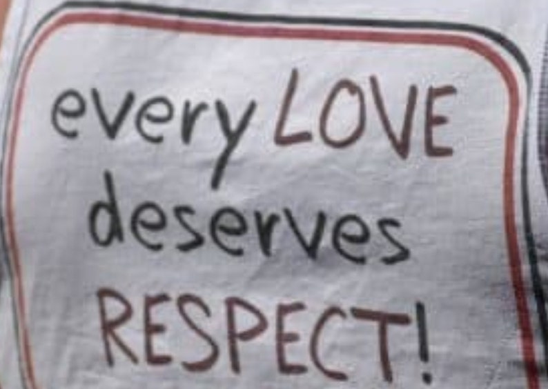 May include: A white sign with a red border and black text that reads "every LOVE deserves RESPECT!"