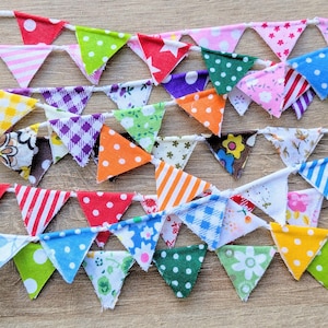 May include: A colourful fabric bunting with a variety of patterns and colours, including red, white, blue, green, yellow, and purple. The bunting is strung on a white string and is perfect for decorating a party or event.