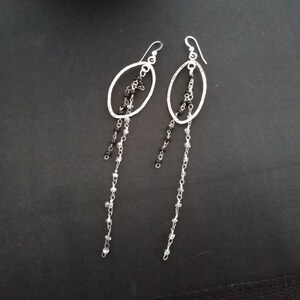 May include: Silver dangle earrings with a textured oval design and black and clear beads hanging from the bottom.