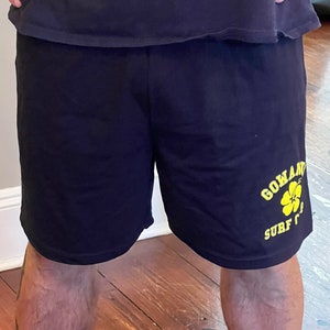 May include: Black athletic shorts with a yellow graphic of a flower and the text "Go and Surf".