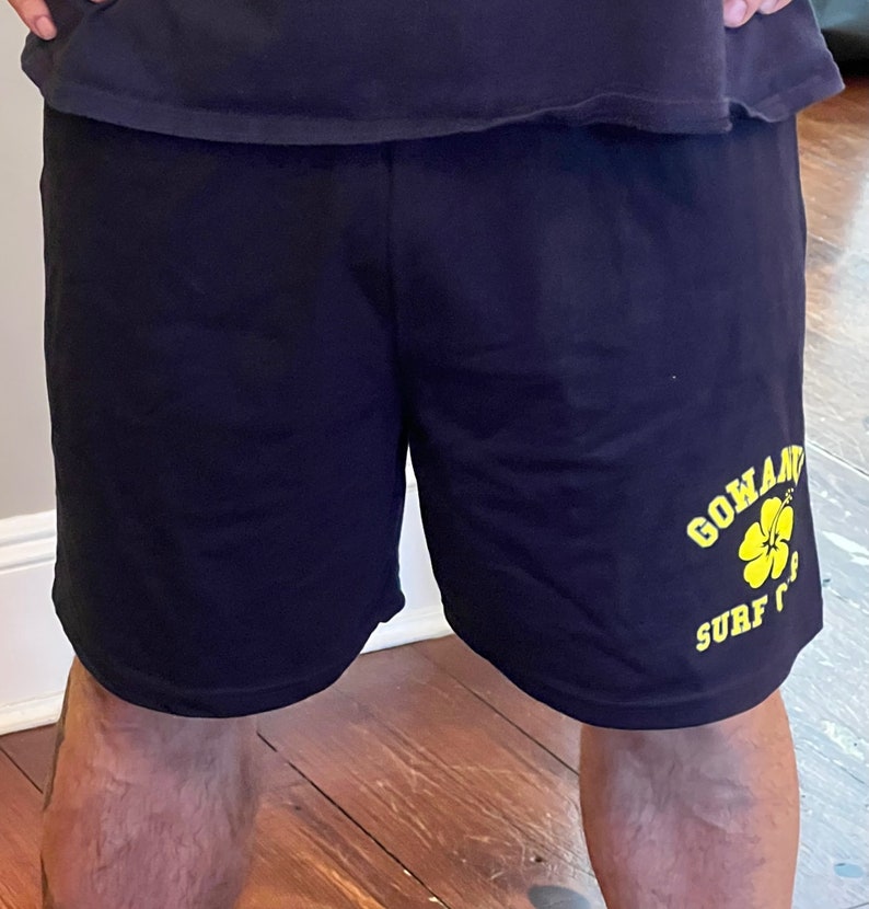 May include: Black athletic shorts with a yellow graphic of a flower and the text "Go and Surf".
