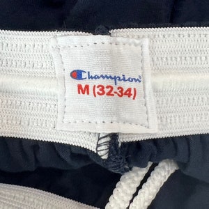 May include: A white tag with black stitching and the text "Champion" and "M (32-34)" on a navy blue fabric background.