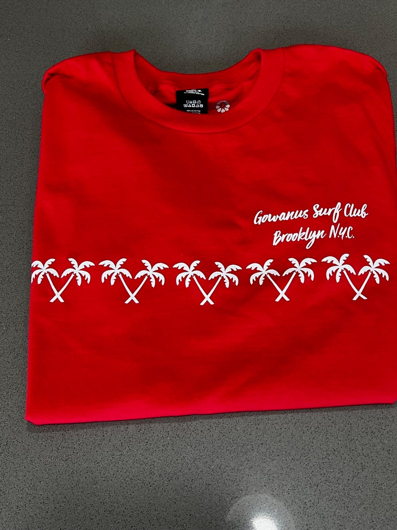 May include: Red t-shirt with a white palm tree design and the text "Gowanus Surf Club Brooklyn NYC."