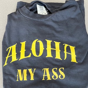 May include: A black t-shirt with the text "ALOHA MY ASS" printed in yellow.