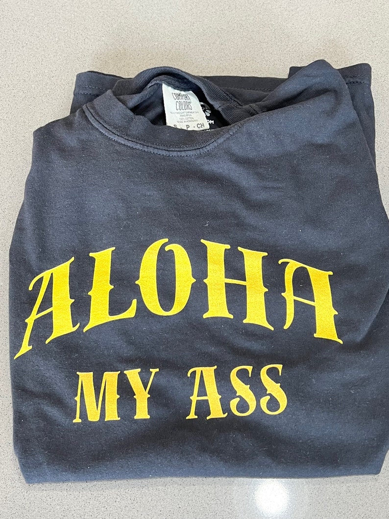 May include: A black t-shirt with the text "ALOHA MY ASS" printed in yellow.