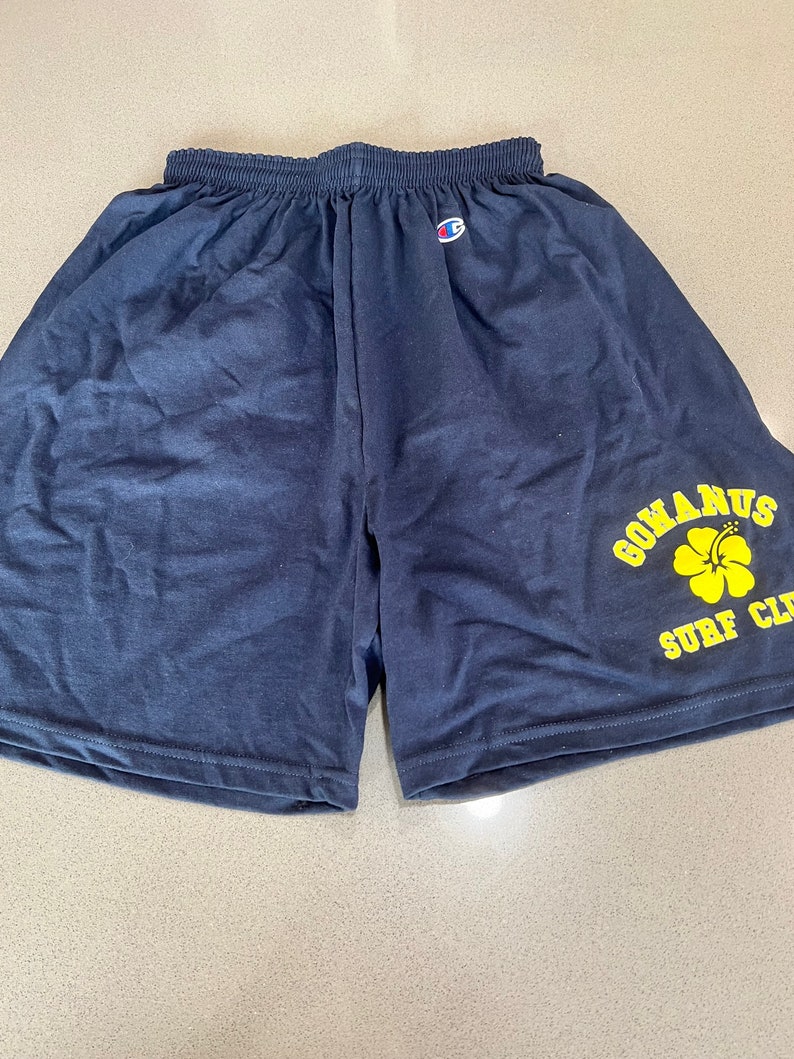 May include: Navy blue Champion athletic shorts with a yellow logo that says "Gomarus Surf Club" and a yellow hibiscus flower.