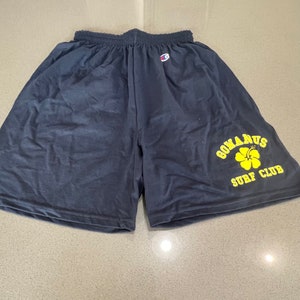May include: Black athletic shorts with a yellow logo that says "GOMANUS SURF CLUB" and a yellow hibiscus flower.