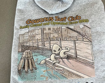 May include: Grey hooded sweatshirt with a graphic print of a cartoon octopus in a boat. The text "Gowanus Surf Club Family Owned and Operated Since 2020" is printed on the sweatshirt. The text "Waiting for the Perfect Wave" and "Brooklyn, New York" is printed below the graphic. A palm tree icon is printed on the right side of the sweatshirt.