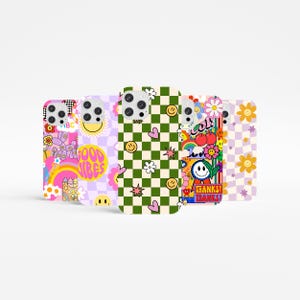 Puede incluir: Cinco fundas de teléfono diferentes con una variedad de diseños coloridos y caprichosos. Los diseños incluyen caras sonrientes, flores, corazones, estrellas y patrones a cuadros. El texto en las fundas incluye "Good Vibes", "Thanks", "Cool" y "ABC".