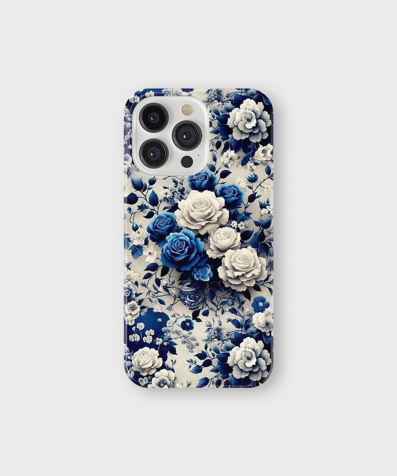 以下が含まれることがあります： 青と白のバラと葉のフローラルデザインの携帯電話ケース。ケースは光沢仕上げで、カメラの切り抜きがあります。フローラルパターンはケースの背面全体を覆っています。
