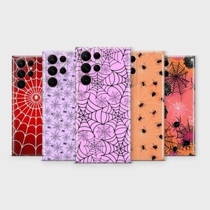 May include: A collection of five phone cases with Halloween-themed designs. The cases feature patterns like spiderwebs and spiders in colors such as red, lavender, pink, and orange. The cases have a glossy finish and are designed for a smartphone.