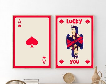 May include: Two framed prints of playing cards. The left print is a red ace of spades. The right print is a red queen of spades with the text "LUCKY YOU" in red.