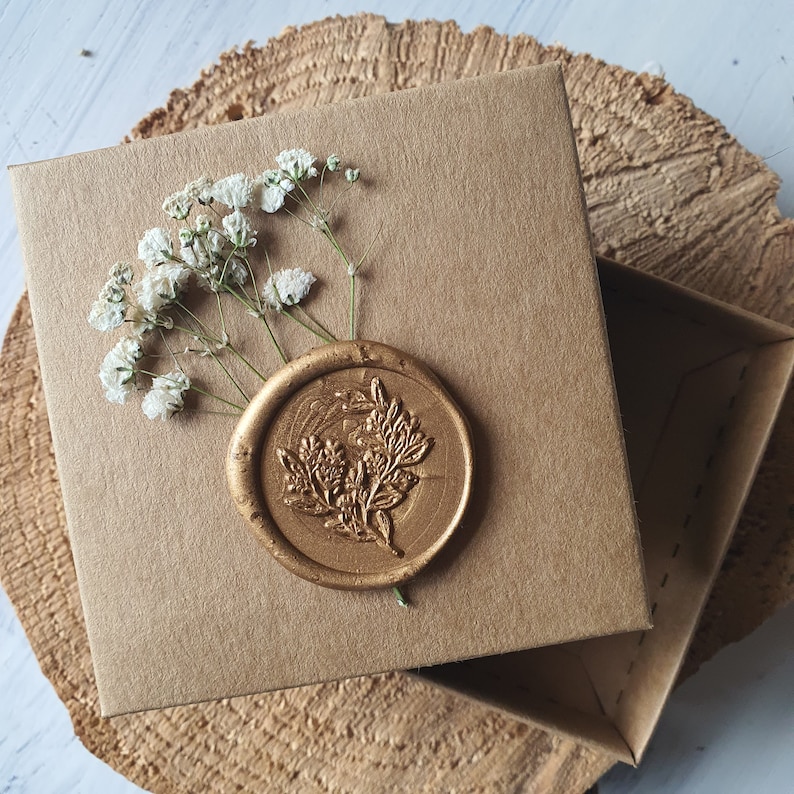 May include: A brown cardboard box with a gold wax seal. The seal has a floral design. The box is decorated with white flowers.