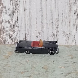 Puede incluir: Un modelo de coche de juguete negro de un convertible clásico con interior rojo. El coche está sobre una superficie de madera blanca.