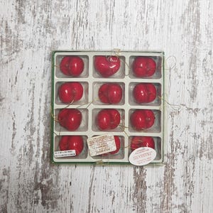 May include: A set of twelve red heart-shaped ornaments packaged in a clear plastic tray. Each ornament has a gold hanging string. A white label on the tray reads Silvestri, and another label states this is not a food product and is a decoration.
