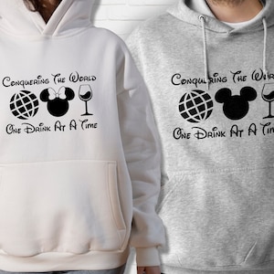 May include: Two white and grey hooded sweatshirts with black text and graphics. The text on the sweatshirts reads "Conquering the World One Drink at a Time". The graphics include a globe, a Mickey Mouse head with a bow, and a wine glass.