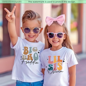 Puede incluir: Dos niños con camisetas blancas con texto colorido y gafas de sol. La camiseta del niño dice "BIG BRO Freddie" y la de la niña "LIL SIS Olivia". La niña lleva un lazo rosa.