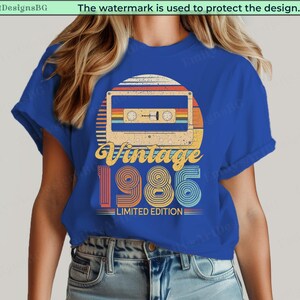 May include: Blue t-shirt featuring a retro design with a cassette tape graphic, a sunset, and the text "Vintage 1985 Limited Edition." The design incorporates orange, yellow, red, and blue colors.