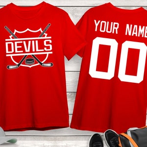 May include: Two red t-shirts, one with the text "DEVILS" and a hockey stick and puck graphic, and the other with the text "YOUR NAME" and the number "00".