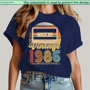 May include: Navy blue t-shirt featuring a retro design with a cassette tape, a sunset, and the text "Vintage 1986 Limited Edition." The design incorporates orange, yellow, and teal colors.