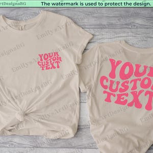 Puede incluir: Dos camisetas beige con el texto "YOUR CUSTOM TEXT" en rosa con fuente retro. Una camiseta tiene el texto en la parte delantera y la otra en la parte trasera.