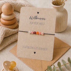 May include: A personalized bracelet with the name "SOPHIA" spelled out in colorful beads. The bracelet is displayed on a card with German text and a small heart symbol. A wooden stacking toy and a small vase are also in the image.
