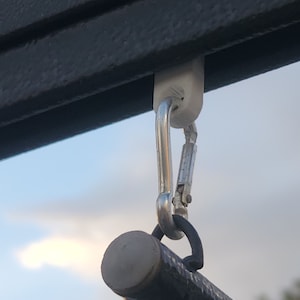 May include: A white plastic clip with a silver carabiner hook attached to a black metal rod.