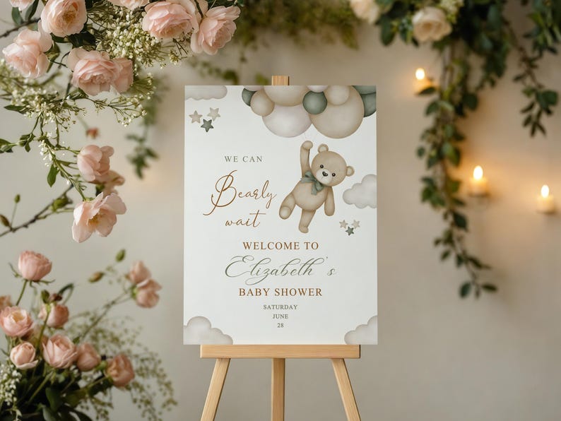 May include: A baby shower welcome sign on an easel. The sign features a teddy bear illustration with the text "We can bearly wait" and "Welcome to Elizabeth's Baby Shower". The sign is decorated with clouds and stars.