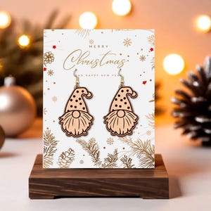 May include: Wooden gnome earrings with black polka dots on the hat and a long, flowing beard. The earrings are displayed on a card that says "Merry Christmas" and "Happy New Year". The earrings are on a wooden stand.