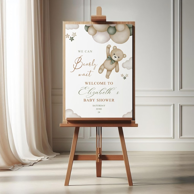May include: A wooden easel displays a baby shower welcome sign. The sign features a teddy bear illustration with the text "We can bearly wait" and "Welcome to Elizabeth's Baby Shower". The sign is decorated with clouds and stars.